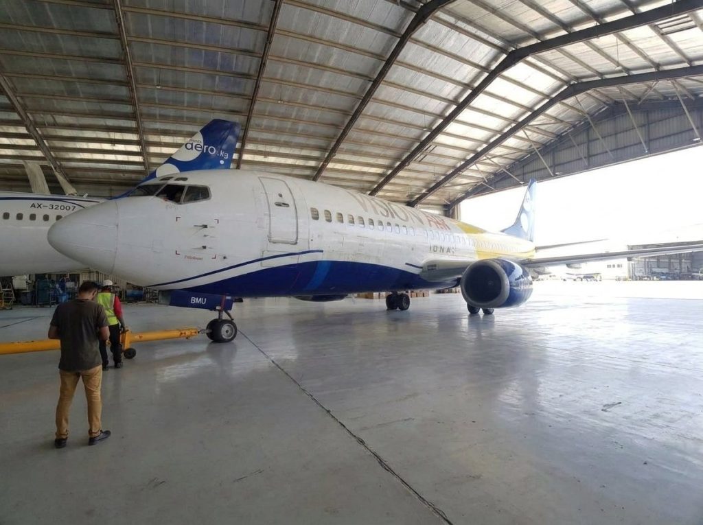 A Boeing 737 in the hangar with the ground crew and tow bar
