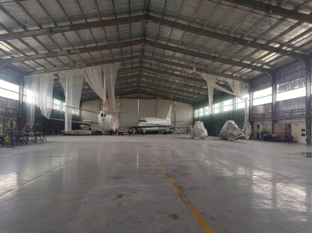Inside the hangar, with aircraft parked for maintenance under the steel roof